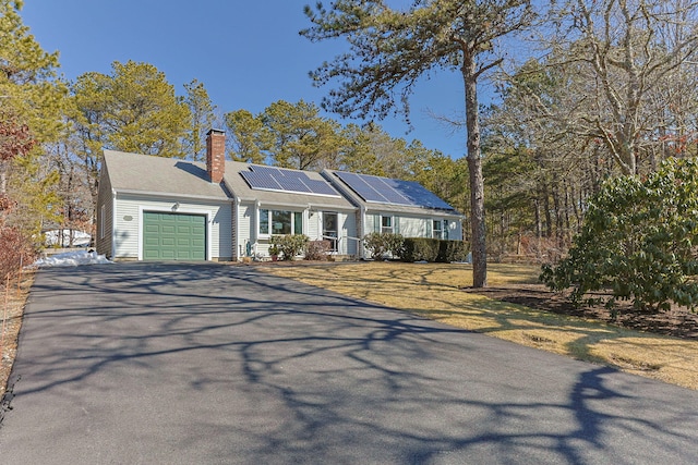 ranch-style house featuring a garage, solar panels, aphalt driveway, and a chimney