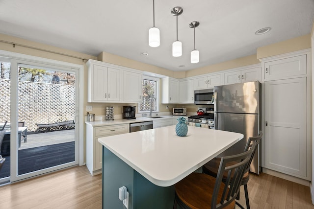 kitchen with white cabinetry, light countertops, appliances with stainless steel finishes, a center island, and decorative light fixtures