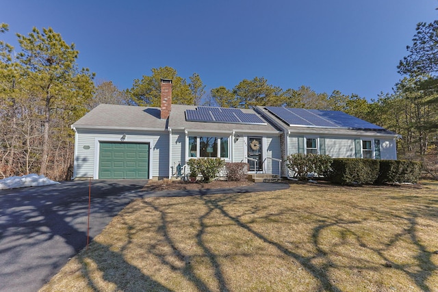 ranch-style home with a garage, driveway, roof mounted solar panels, a front lawn, and a chimney