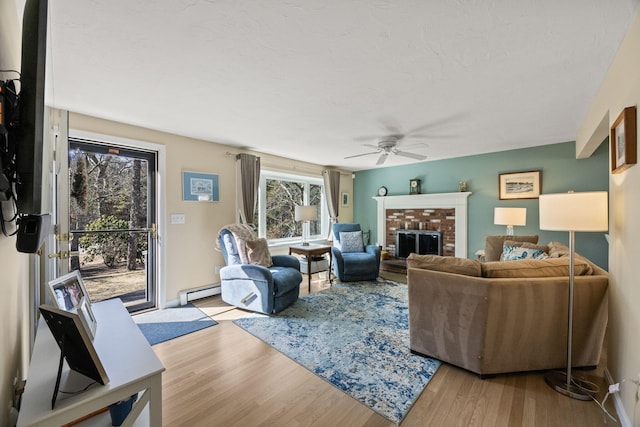 living area with light wood-type flooring, a brick fireplace, ceiling fan, and baseboard heating