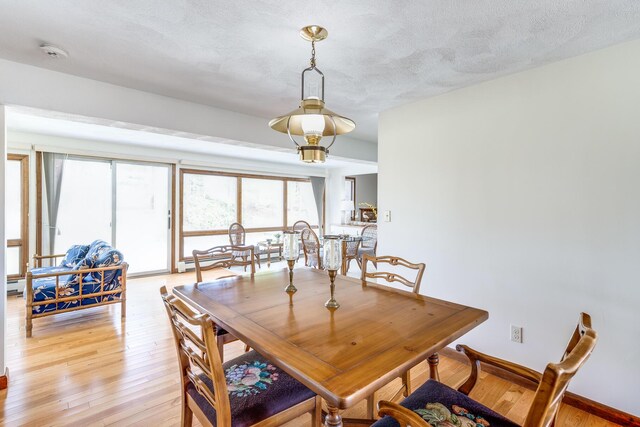 dining space with light wood-type flooring, a textured ceiling, and baseboards