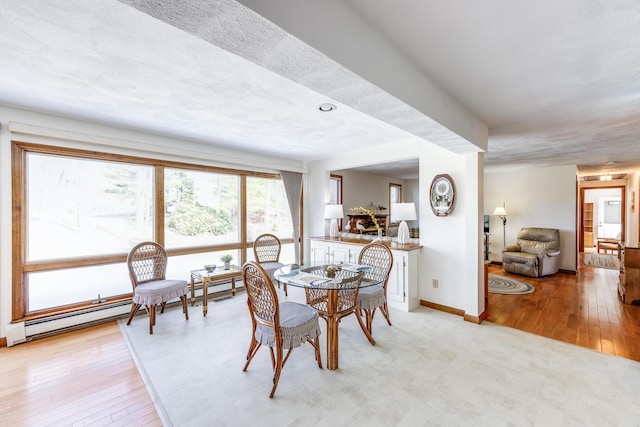 dining area featuring a baseboard heating unit, light wood-style flooring, and baseboards