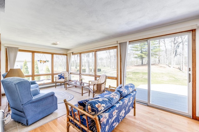 living room featuring plenty of natural light, light wood-type flooring, baseboard heating, and a textured ceiling