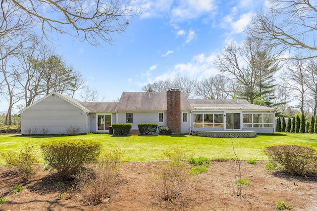 back of house with a sunroom, a chimney, and a lawn