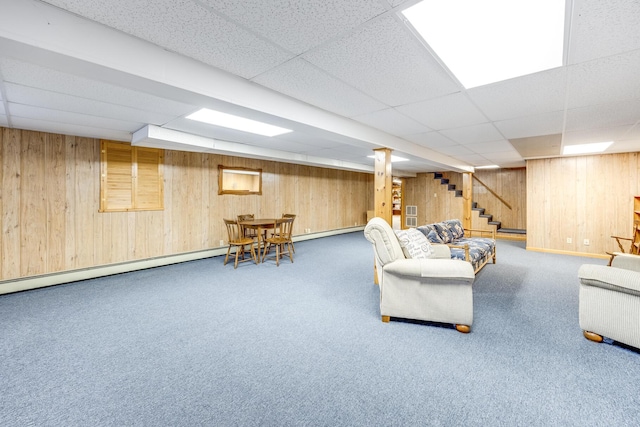 living area featuring a drop ceiling, stairway, wood walls, a baseboard radiator, and carpet