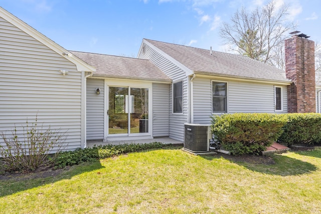 back of property featuring central AC unit, a yard, and roof with shingles