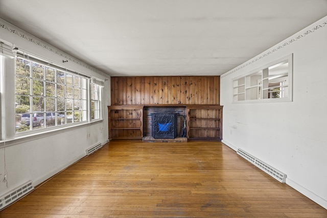 unfurnished living room featuring a fireplace, a baseboard heating unit, wood-type flooring, baseboards, and wooden walls