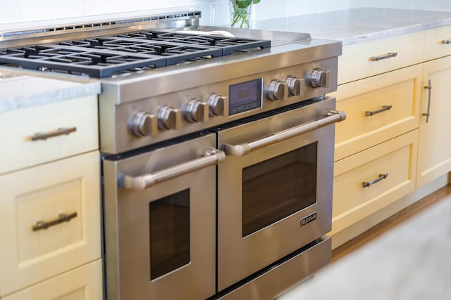 interior details featuring decorative backsplash, light stone countertops, and range with two ovens