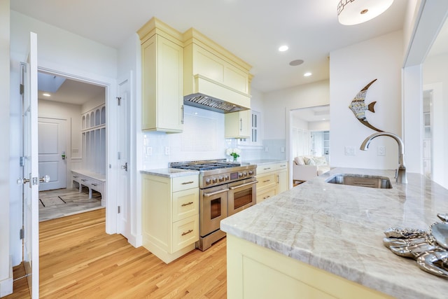 kitchen featuring light stone countertops, range with two ovens, light hardwood / wood-style floors, sink, and cream cabinetry