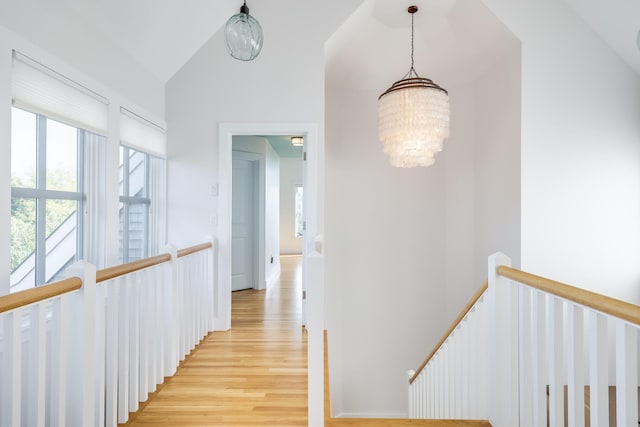 corridor with light wood-type flooring, vaulted ceiling, and an inviting chandelier