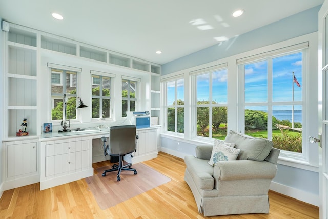 office area with a water view, a healthy amount of sunlight, built in desk, and light wood-type flooring