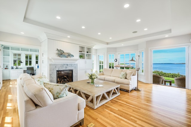 living room featuring a healthy amount of sunlight, light wood-type flooring, a premium fireplace, and a raised ceiling