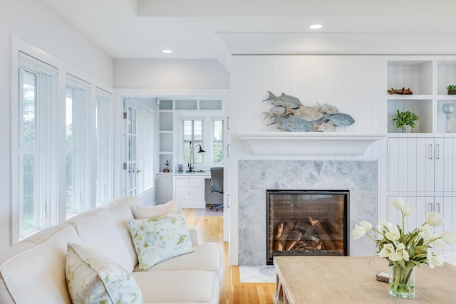 living room with built in shelves, a high end fireplace, and light hardwood / wood-style floors