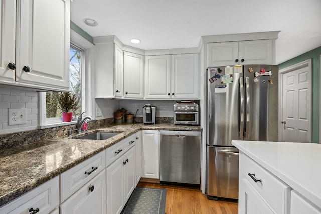 kitchen featuring appliances with stainless steel finishes, a sink, light wood finished floors, tasteful backsplash, and recessed lighting