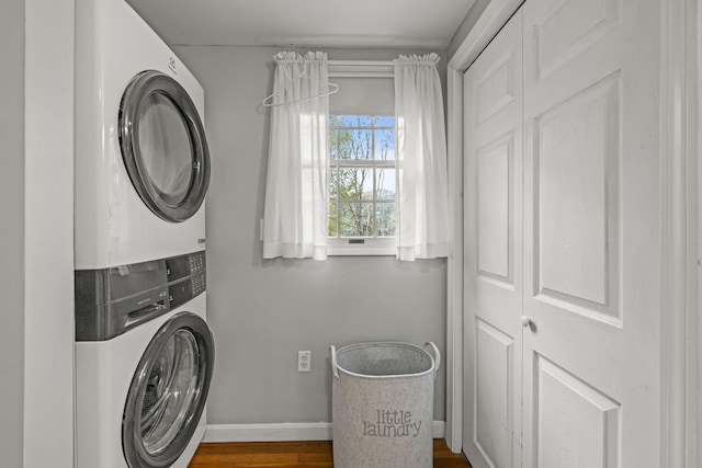 clothes washing area with stacked washing machine and dryer, baseboards, and dark wood finished floors