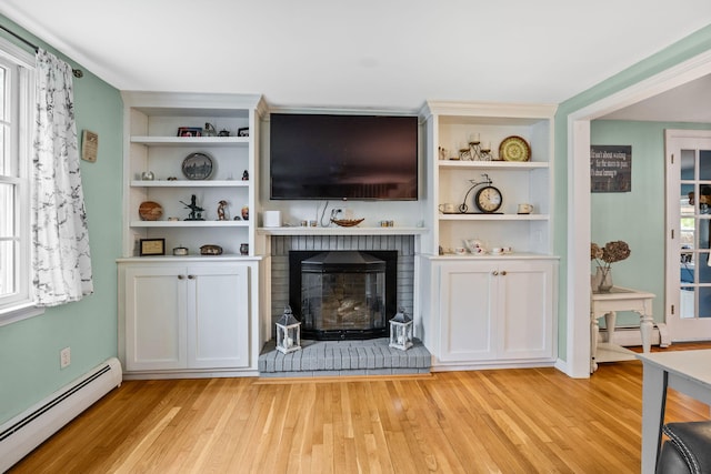 living room featuring a baseboard heating unit, light wood-type flooring, built in shelves, and a brick fireplace