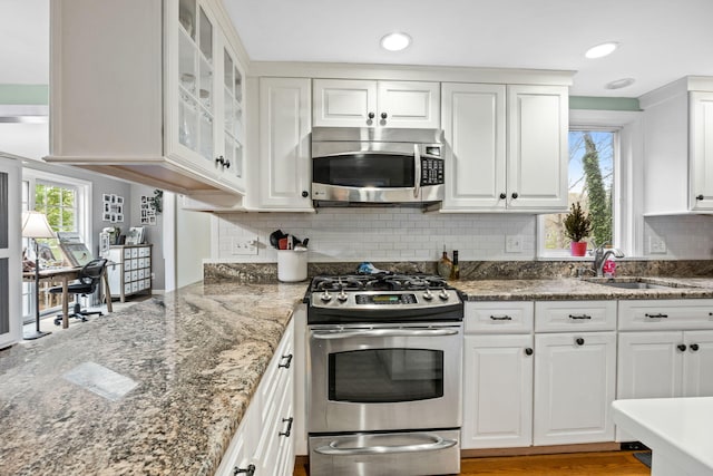 kitchen with stainless steel appliances, a sink, white cabinets, backsplash, and recessed lighting