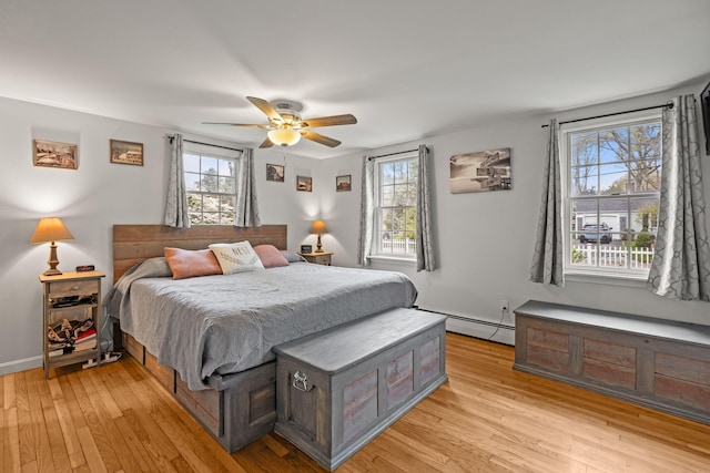bedroom with a baseboard heating unit, multiple windows, and light wood-style floors