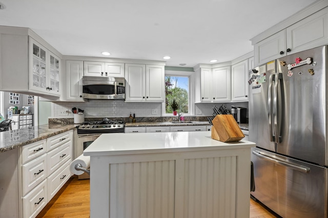 kitchen with appliances with stainless steel finishes, a sink, backsplash, white cabinetry, and glass insert cabinets