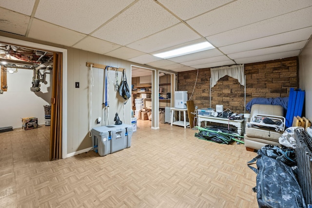 finished below grade area featuring a paneled ceiling, wooden walls, and baseboards