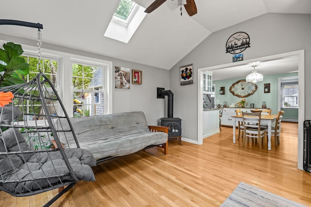 living area with a wood stove, vaulted ceiling, a ceiling fan, and light wood-type flooring