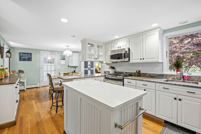 kitchen featuring appliances with stainless steel finishes, a baseboard heating unit, a sink, a center island, and light wood finished floors