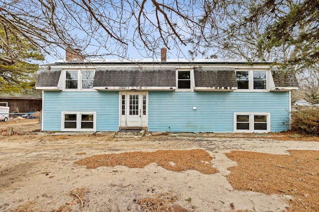 rear view of house with a shingled roof, entry steps, and a chimney