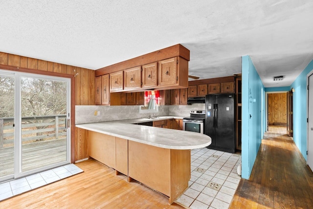 kitchen with freestanding refrigerator, electric range, a peninsula, under cabinet range hood, and light countertops