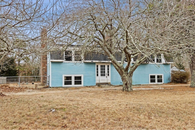 rear view of property featuring fence, entry steps, a chimney, and a lawn