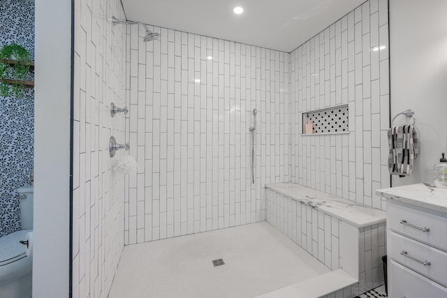 bathroom with a tile shower, toilet, and vanity