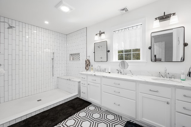 bathroom featuring double vanity, visible vents, tiled shower, and a sink