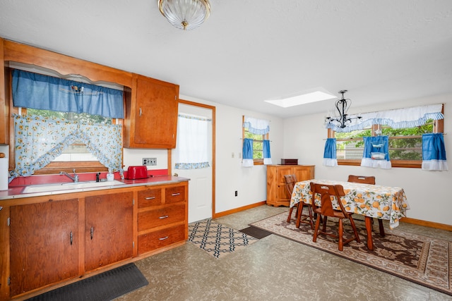 64 Uncle Percys Rd, Mashpee, MA 02649 - kitchen featuring a chandelier, baseboards, brown cabinetry, a skylight, and a sink