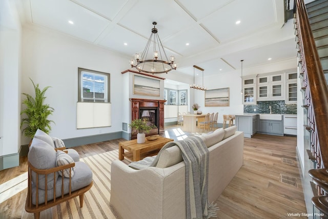 living room featuring coffered ceiling, sink, a notable chandelier, and light wood-type flooring