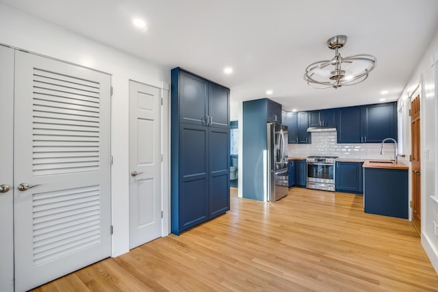 kitchen with pendant lighting, stainless steel appliances, butcher block counters, a sink, and blue cabinets