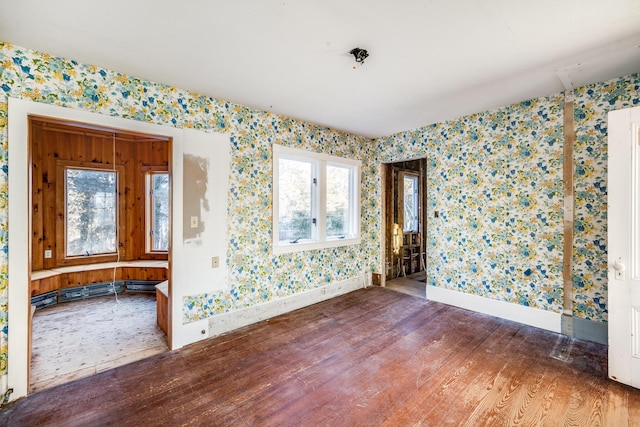 empty room with wallpapered walls, a wealth of natural light, and wood finished floors