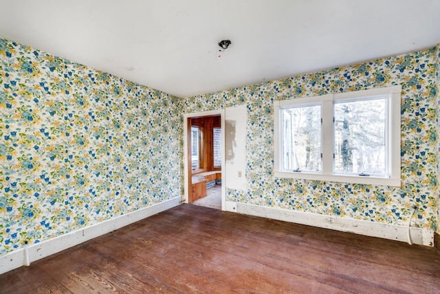 spare room featuring wallpapered walls, baseboards, and dark wood-type flooring