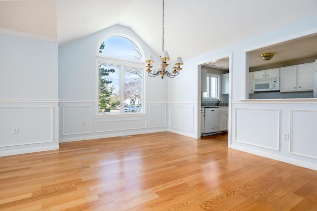 unfurnished dining area with vaulted ceiling, a wainscoted wall, light wood finished floors, an inviting chandelier, and a decorative wall