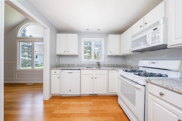 kitchen with light wood-style floors, a sink, a healthy amount of sunlight, and white appliances