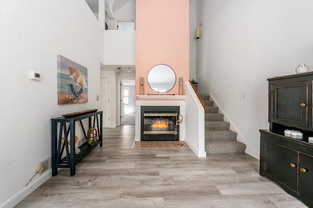 interior space featuring a towering ceiling, light wood-type flooring, stairway, baseboards, and a glass covered fireplace