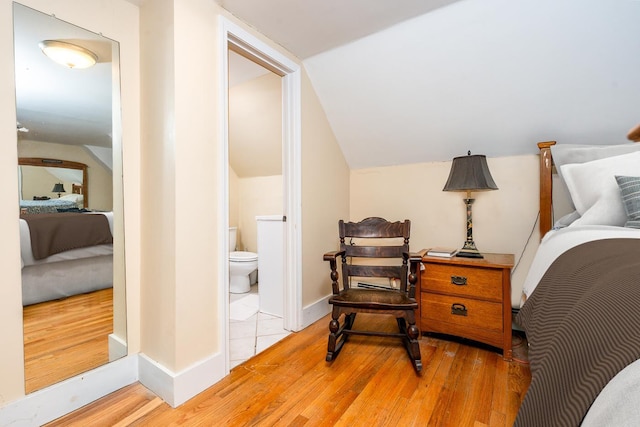 bedroom with vaulted ceiling, ensuite bath, and hardwood / wood-style floors