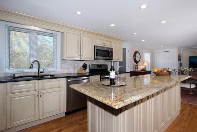 kitchen with stainless steel appliances, a sink, plenty of natural light, wood finished floors, and cream cabinets