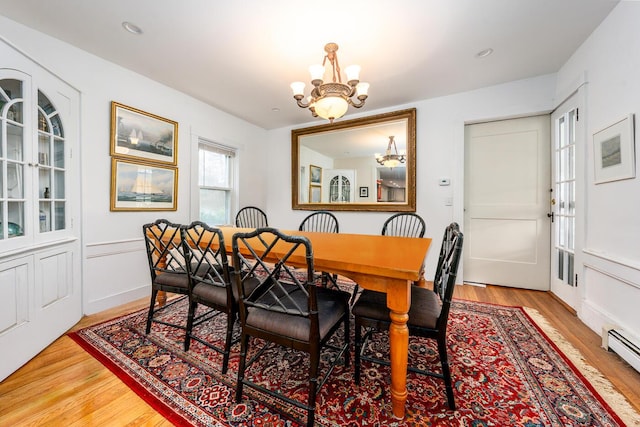 dining space with baseboard heating, an inviting chandelier, and light wood-style floors