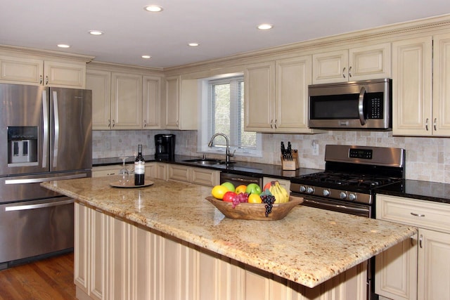 kitchen with cream cabinetry, light stone counters, stainless steel appliances, a sink, and a center island