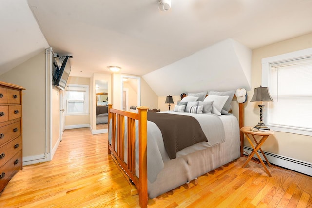 bedroom featuring a baseboard heating unit, vaulted ceiling, baseboards, and light wood-style floors