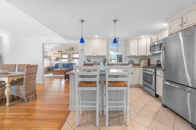 kitchen featuring decorative light fixtures, light wood finished floors, a breakfast bar area, appliances with stainless steel finishes, and a kitchen island