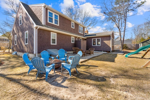 rear view of property with an outdoor fire pit, fence, a playground, and a yard