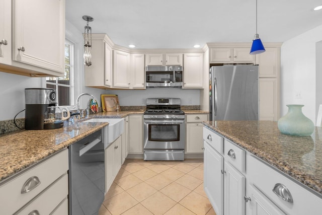 kitchen with decorative light fixtures, stainless steel appliances, light tile patterned flooring, a sink, and dark stone countertops