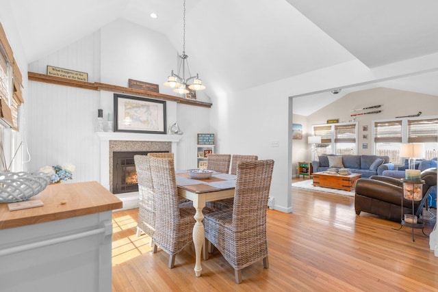 dining room featuring high vaulted ceiling, a glass covered fireplace, light wood-style flooring, and an inviting chandelier