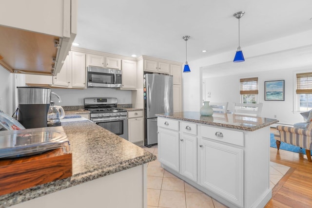 kitchen featuring white cabinets, a kitchen island, appliances with stainless steel finishes, decorative light fixtures, and stone counters