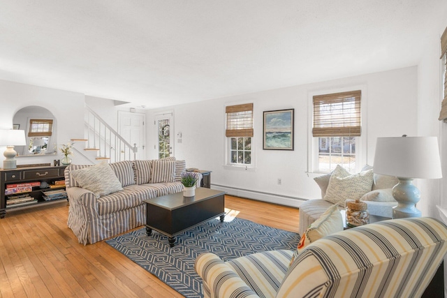 living room featuring light wood finished floors, a baseboard radiator, and stairs